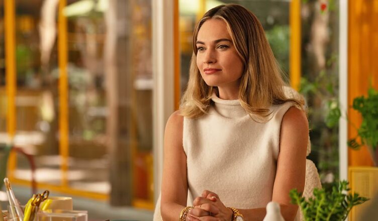 A woman in a white sleeveless turtleneck sitting indoors with a thoughtful expression.
