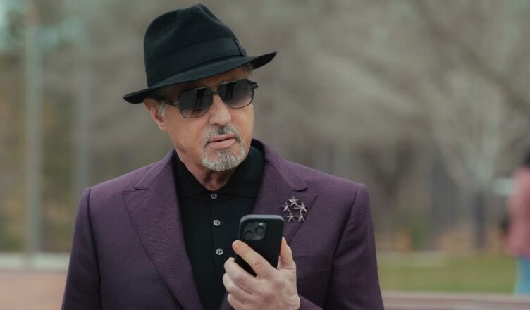 Stylish older man in a hat and sunglasses checks his phone outdoors.