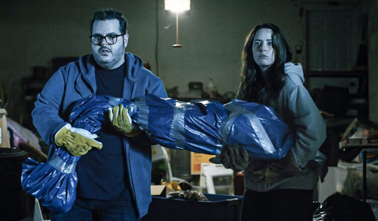Two forensic investigators handling a body bag in a dimly lit lab.