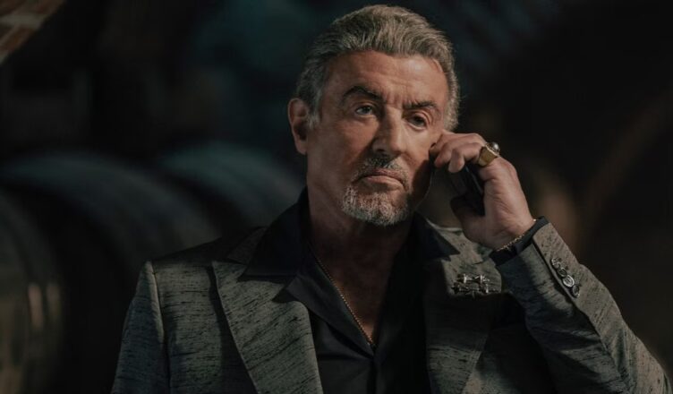 A contemplative man with a beard and styled hair in dark attire.