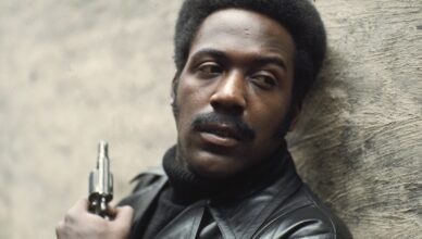 Man holding a gun, looking serious and alert.