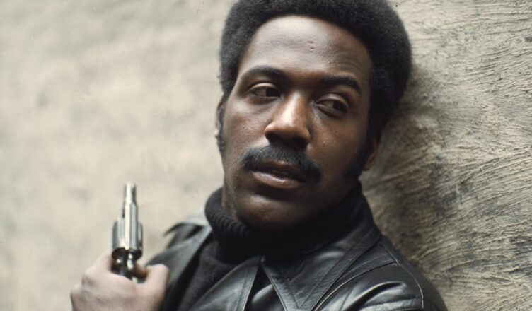 Man holding a gun, looking serious and alert.