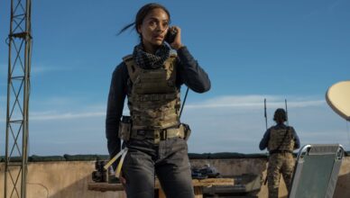 Lioness Series Hub image featuring Zoe Saldaña as Joe in tactical gear sitting in a desert war zone during a covert CIA mission