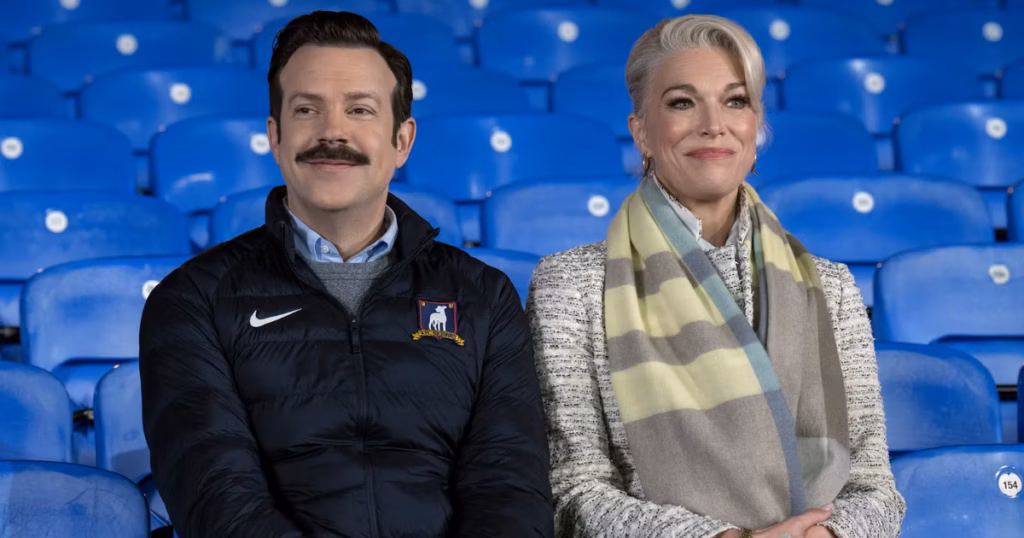 Ted Lasso Episode 401 Preview image from "Home" featuring Ted Lasso and Rebecca Welton seated at AFC Richmond as Season 4 begins.