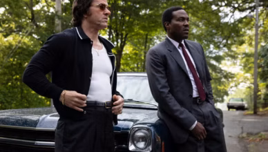 By Any Means stars Mark Wahlberg as Greg Scarpa and Yahya Abdul-Mateen II as FBI Agent Wayne Strider standing beside a vintage car.